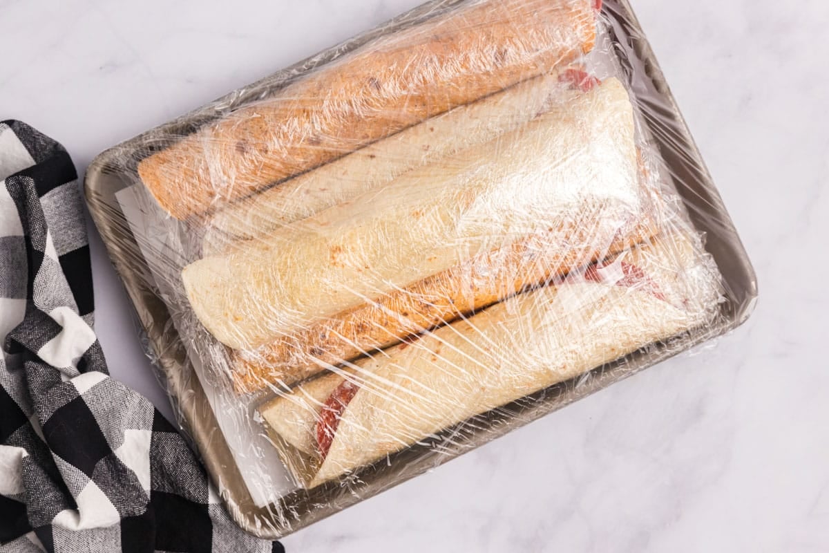 rolled tortillas covered in plastic wrap on a table