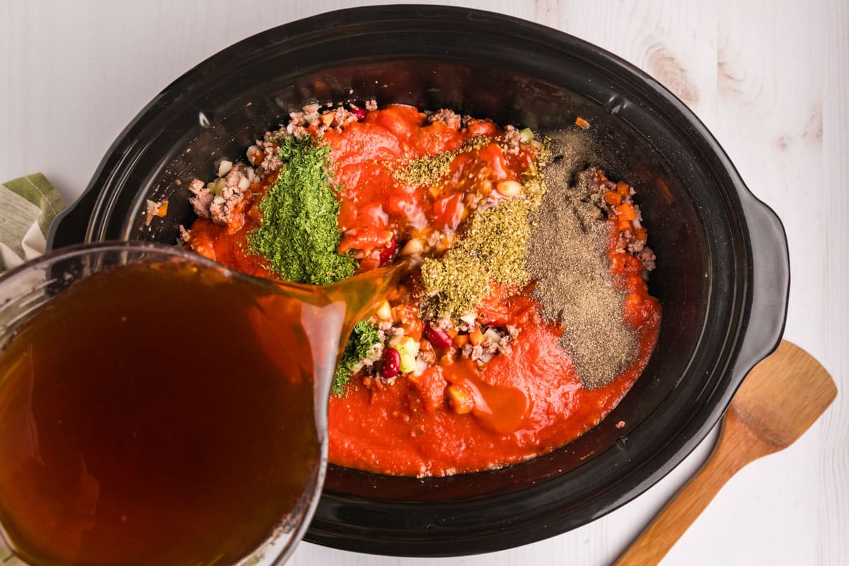 pouring beef broth into a crockpot of soup ingredients