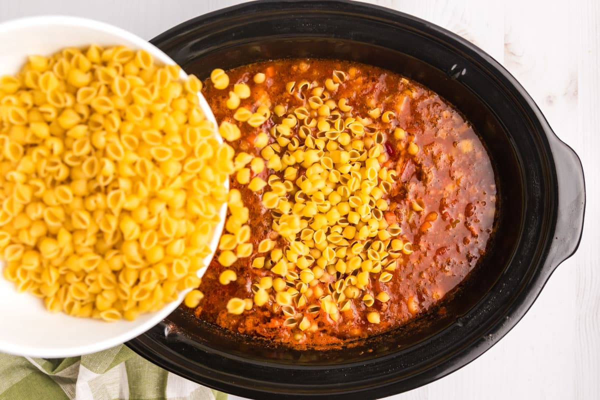pouring dry pasta into a crockpot of soup
