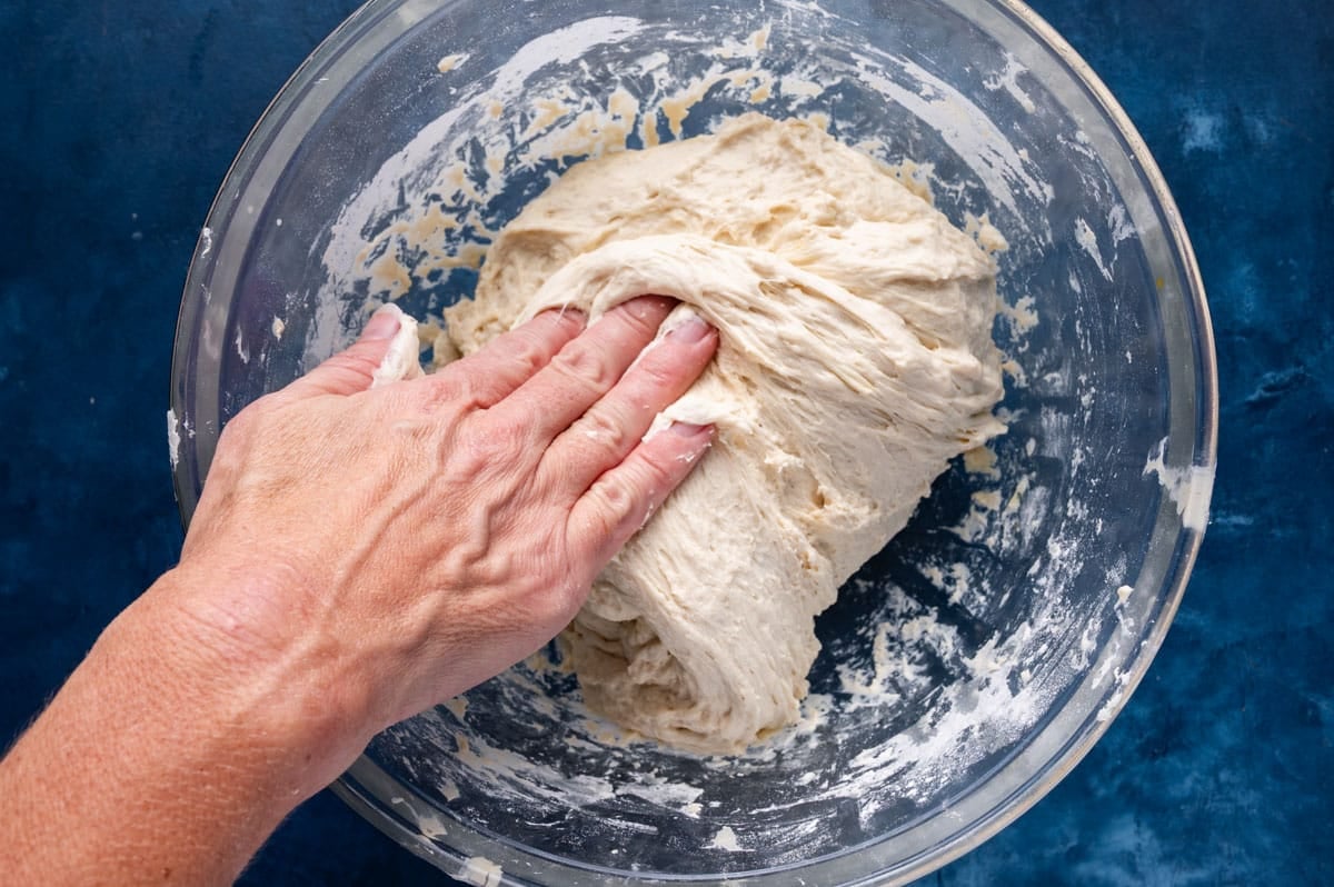 a handing folding dough in a glass bowl