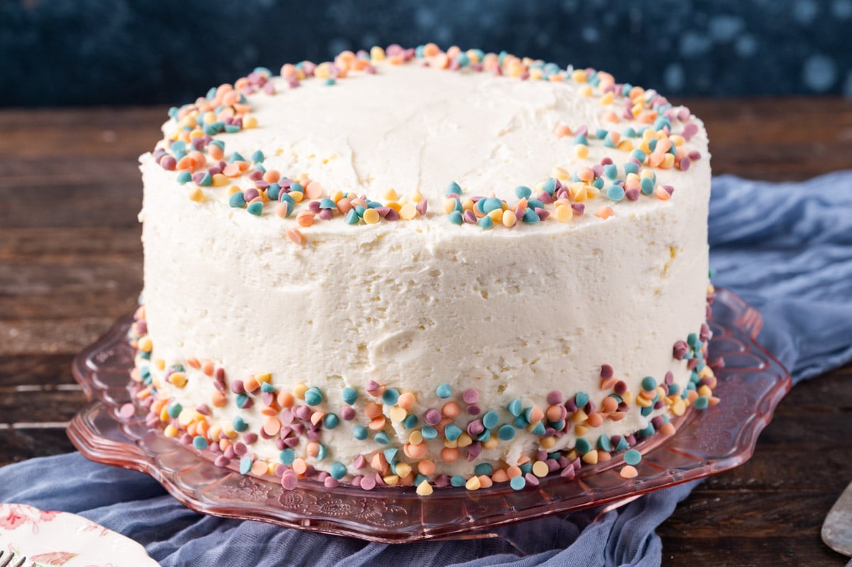 a layered cake with white frosting and rainbow chip sprinkles