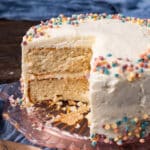 a two layer birthday cake with white frosting, with a slice cut out