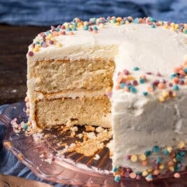 a two layer birthday cake with white frosting, with a slice cut out