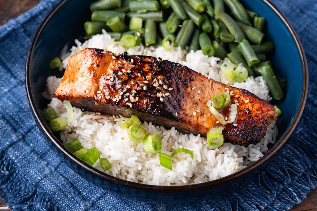 a piece of honey garlic salmon on a bed of rice with green beans