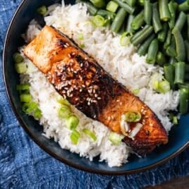 a piece of cooked salmon on a bed of rice with green beans