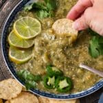 a hand dipping a chip into salsa verde