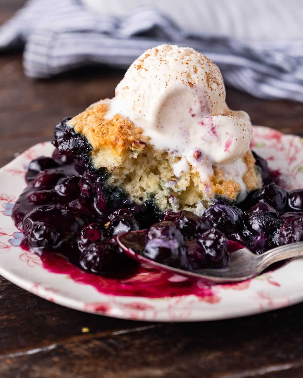a serving of blueberry cobbler a la mode on a plate with a spoon